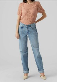 Hellrosa strukturiertes Oberteil mit Puffärmeln, kombiniert mit hellblauen, zulaufenden Jeans, an den Knöcheln umgeschlagen, und beigen spitzen Absatzschuhen.