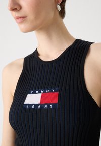 Juodas šonkačių viršus su ryškiu logotipo užkliju ir raudonais, baltais bei mėlynais akcentais. Lygi tekstūra ir prigludęs dizainas.