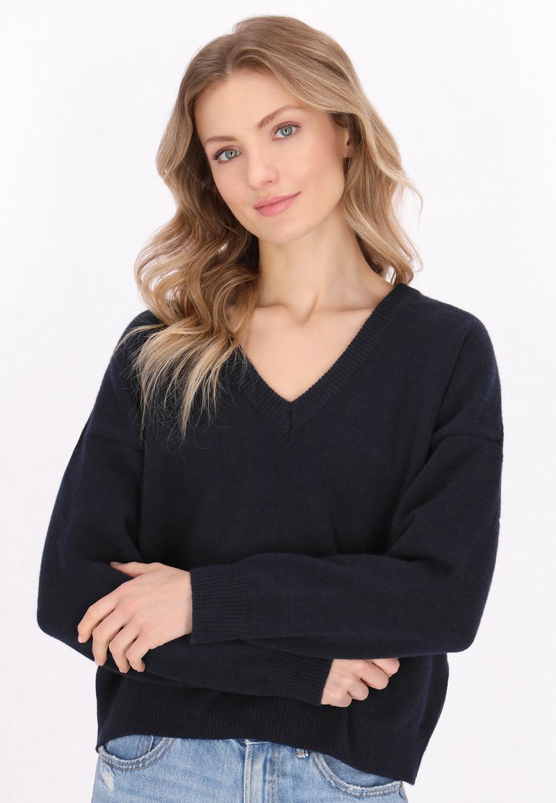 Granatowy sweter w serek wykonany z miękkiej dzianiny, z długimi, luźnymi rękawami i ściągaczami. Design jest swobodny i casualowy.