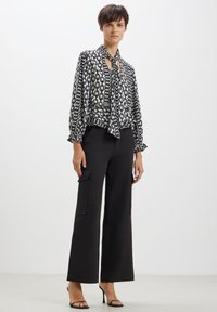 Blusa bianca e nera con motivo a catena, colletto a fiocco e polsini elastici, abbinata a pantaloni neri a vita alta e gamba larga con tasche cargo.