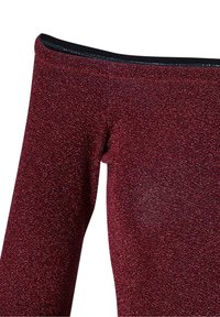 Gros plan sur un tissu brillant pailleté rouge foncé formant une partie d'un pantalon ajusté ou legging avec une ceinture noire.