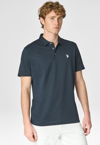Polo blu navy in misto cotone con colletto classico, tre bottoni e logo ricamato sul petto; texture liscia e maniche corte.
