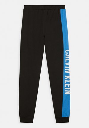 Pantalones jogger negros con franja lateral azul que presenta texto vertical blanco "Calvin Klein" en una pierna y cintura y puños elásticos.