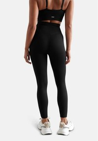 Top corto nero a coste e leggings a vita alta. Texture liscia con un design aderente. Indossato con sneakers bianche, che mostrano uno stile sportivo.