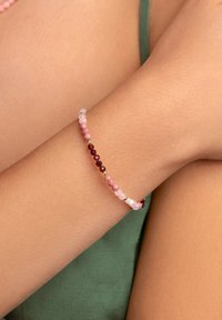 Pulsera de cuentas hecha de piedras de varios colores en tonos de rosa y rojo, intercaladas con pequeños acentos dorados. Presenta cuentas lisas y texturizadas.