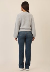 Maglione grigio a maglia con texture a coste, maniche a sbuffo e orlo aderente, abbinato a jeans svasati blu scuro e sneakers bianche.