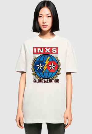 Hvid oversized t-shirt med iøjnefaldende grafisk print med blå og røde elementer, stjerner, en globe og teksten "INXS CALLING ALL NATIONS."