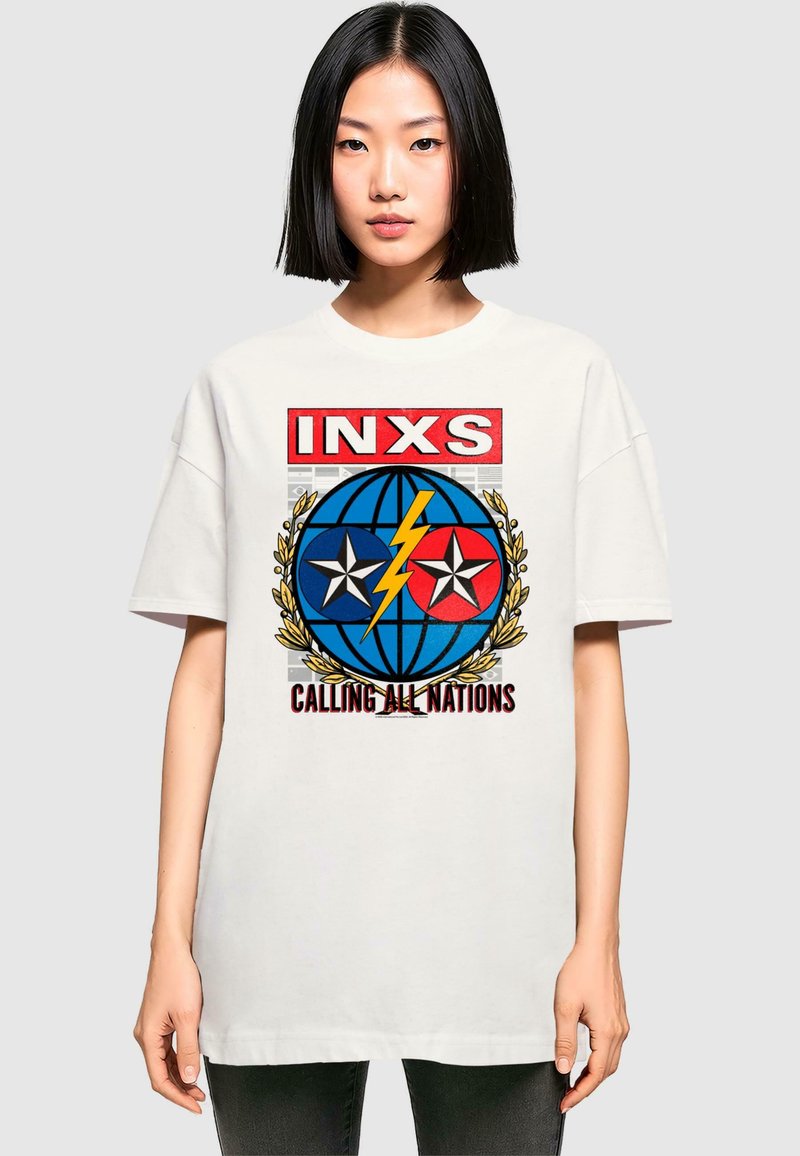 Vit oversized t-shirt med djärv grafiktryck som har blå och röda element, stjärnor, en jordglob, och texten "INXS CALLING ALL NATIONS."