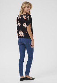Black floral blouse with short sleeves, featuring pink and white flowers. Paired with blue skinny jeans and black flats. Simple design.