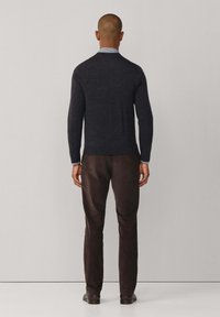 Donkergrijze lange mouwen trui met een ronde hals, gemaakt van een zachte stof, gecombineerd met donkerbruin broek en zwarte schoenen.