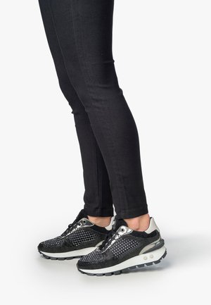 Scarpe sportive nere con accenti metallici, parte superiore in rete e motivo a pois. Suola spessa con battistrada testurizzato. Abbinato a jeans neri attillati.