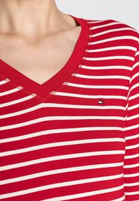 Rot-weißer gestreifter Langarmshirt mit V-Ausschnitt. Besitzt ein kleines Markenlogo auf der Brust. Material scheint weich und figurbetont.