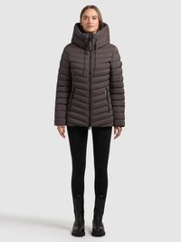 Puhasta jakna tamno smeđe boje s okomitom prošivenom uzorkom, visokim ovratnikom i zatvaračem sprijeda. Nošena preko crnih tajica i čizama.