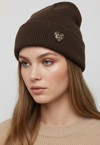 Brown knit beanie with ribbed texture and a leopard-print heart-shaped patch accent. Soft, warm material with a snug design.