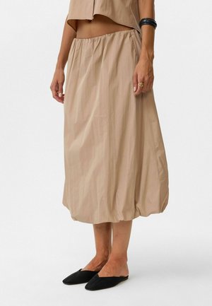 Beige, knie-lange rok met een elastische tailleband en een geplooid, volumineus ontwerp. De stof is lichtgewicht en heeft een lichte kreukeling.