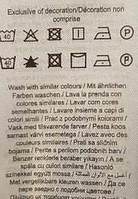 Priežiūros etiketė, kurioje yra skalbimo simboliai ir daugiausia kalbų skalbimo nurodymai. Etiketė pagaminta iš šviesios spalvos audinio su juodu spaudiniu.