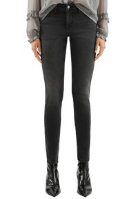 Wąskie czarne jeansy z denimu z wysokim stanem. Charakteryzują się klasycznym wzorem z pięcioma kieszeniami i subtelnym efektem sprania, zestawione ze spiczastymi czarnymi butami.