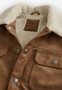 Jachetă din suede artificial, de culoare maro, cu guler din sherpa crem, nasturi tip snap și buzunare frontale. Eticheta din interior indică "NEXT," mărimea M. Textură moale.