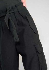 Zwarte cargo broeken van ademend materiaal, met een trekkoord in de taille, zijzakken en een losse pasvorm voor comfort en praktisch gebruik.