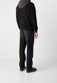 Sudadera negra con capucha y forro gris, combinada con vaqueros negros de corte holgado y zapatillas marrones, con un ajuste relajado y un diseño simple.