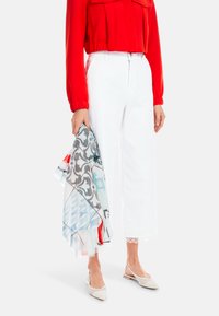 Red long-sleeve blouse with pleats, white cropped pants with lace trim, holding a patterned scarf in blue and red tones, and beige slip-on shoes.