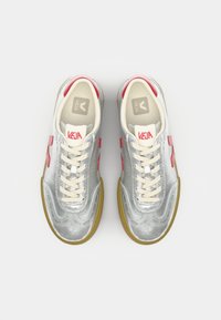Silver sneakers with a shiny texture, cream laces, and red accents. Features a rubber sole and a logo on the tongue and side.
