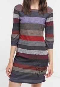 Robe rayée avec des lignes horizontales en rouge, gris, violet et noir, dotée d'un col arrondi et de manches trois-quarts. Détails en découpe laser remarquables à l'ourlet.