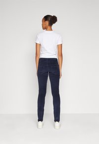 Pantaloni in corduroy blu navy con una vestibilità aderente, caratterizzati da una texture liscia e tasche posteriori, abbinati a una t-shirt bianca a maniche corte.