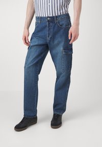 Blå denim cargo bukser med en afslappet pasform, der har sidelommer, en knaplukning og en subtil farvefading. Sorte sko komplimenterer looket.