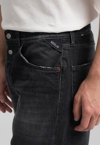 Czarne dżinsy o slim fit, z wyblakłą teksturą, srebrnym wykończeniem i widoczną metką marki na przedniej kieszeni.