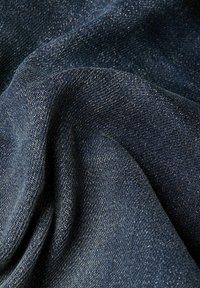 Tume sinine denimkangas pehmea tekstuuriga, millel on kerge läige ja nähtav kude, korraldatud õrnasse voldidesse.