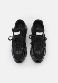 Paire de baskets noires à lacets avec des accents brillants et des semelles épaisses, vue de dessus sur fond blanc.