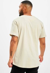 Beige katoenen t-shirt met korte mouwen, ontspannen pasvorm en ronde hals. Glad textuur en subtiele stikseldetails.
