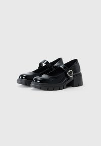 Czarne, lakierowane buty typu Mary Jane z okrągłym noskiem, niskim obcasem, regulowanym paskiem i detalem w kształcie serca na klamerce.