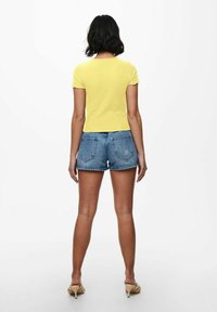 Gelbes, geripptes Kurzarmoberteil mit Rundhalsausschnitt, kombiniert mit blauen Jeansshorts mit fransigem Saum und Gesäßtaschen.