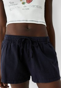 Námořnické modré šortky s elastickým pasem a šnůrkou. Vyrobeno z lehkého materiálu, s bočními kapsami a uvolněným střihem.
