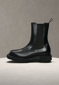Bottine noire en cuir avec semelle épaisse nervurée et empiècement latéral élastique, présentée sur une surface neutre devant un fond gris.