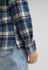 Blauwe en zwarte geruite flanellen shirt met een knoopmanchet, voorzien van een gestructureerde stof en een zijopening, gecombineerd met lichtblauwe jeans.