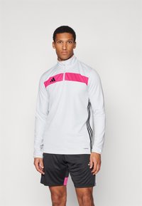 Haut de sport pour homme en gris clair avec un panneau rose et des accents noirs. Il possède un col à zip quart et un tissu texturé avec des manches longues.