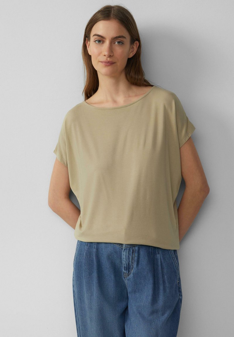 Lichtbeige kortmouwtop met een losse pasvorm, ronde halslijn en een gladde textuur, gecombineerd met hoog-waisted blauwe denim broek.