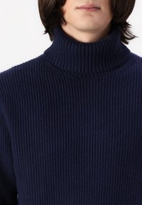 Marineblauer gerippter Rollkragenpullover mit hohem Kragen. Der Stoff hat eine weiche Textur und durchgehende vertikale Streifen.