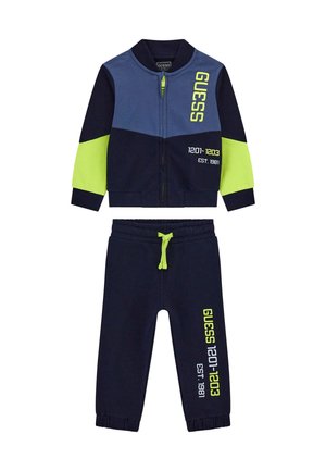 Completo tuta blu navy composto da giacca con zip e dettagli verdi e grafiche, abbinato a pantaloni della tuta coordinati. Realizzato in tessuto morbido.