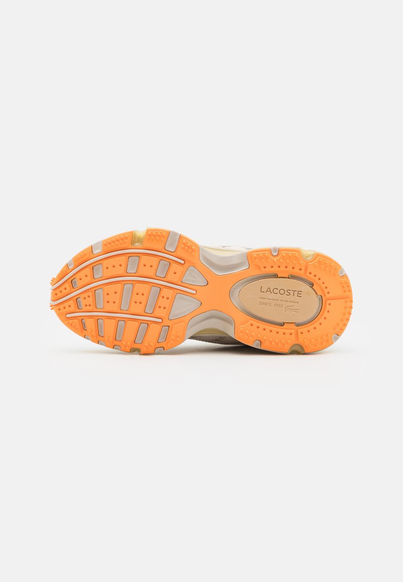 Suela de zapatilla Lacoste, con una parte inferior de goma naranja con patrón, amortiguación gris y un upper beige con la marca en el centro.