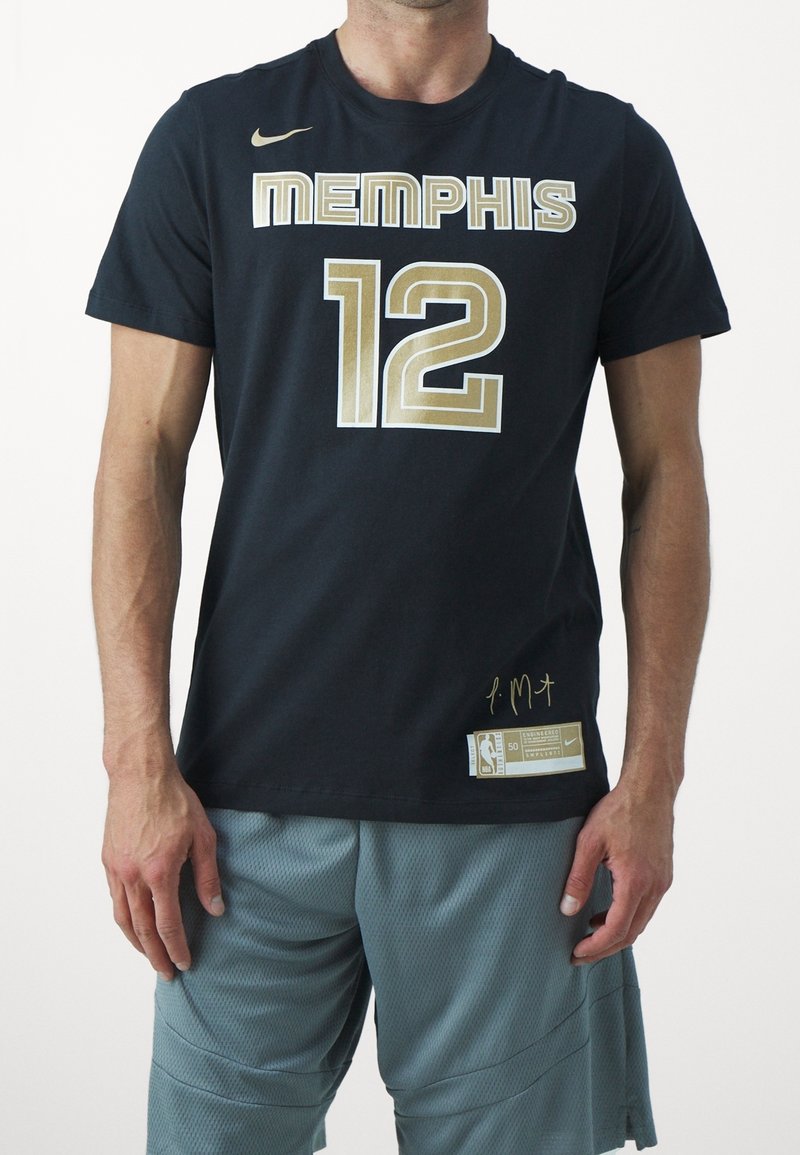 Homme portant un t-shirt de basketball Memphis noir avec le numéro 12 doré et un short de sport gris, debout les bras détendus le long du corps.