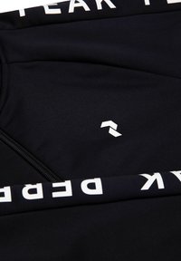 Sort atletisk top lavet af glat stof med lynlås og hvidt logo-detalje. Teksten på ærmerne siger "PEAK PERFORMANCE."