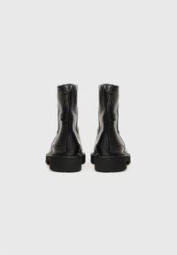 Bottines en cuir noir avec une semelle épaisse prononcée, dotées d'une fermeture éclair arrière et d'un détail en frange sur la tirette de la fermeture.