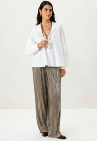 Witte blouse met gerimpelde details, gecombineerd met losse, metallic geplooide zilveren broek. Accessoires omvatten gelaagde kettingen en gouden oorbellen.