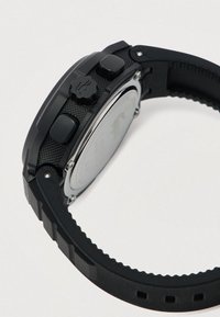 Zwarte digitale polshorloge met een gestructureerde rubberen band, twee zijknoppen en een geribbeld kroon op een lichte achtergrond.