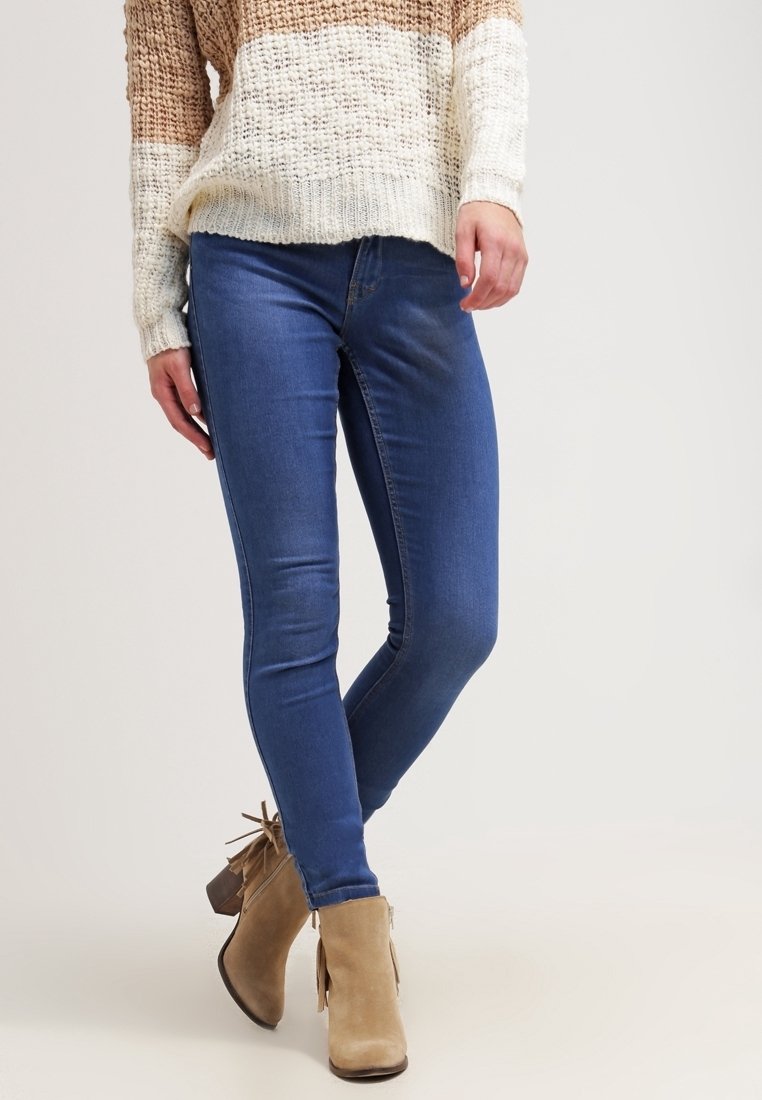 Jean skinny en denim bleu associé à un pull en tricot beige et marron rayé, avec une coupe ample et une finition texturée.