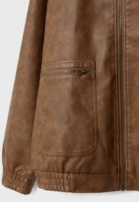 Chaqueta marrón de cuero sintético con cremallera frontal, bolsillo lateral con cremallera, puños elásticos y detalle en el dobladillo.